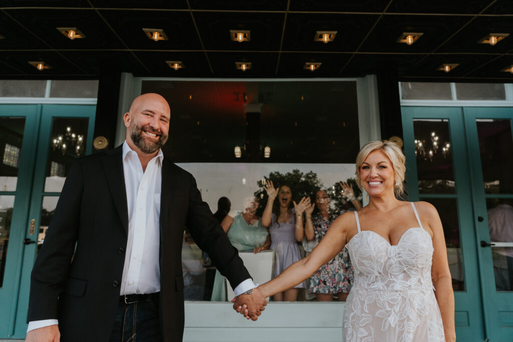 couple grand exit outside the brandt 1910 in wallis tx with reception guests behind them through large windows couple grand exit outside the brandt 1910 in wallis tx with reception guests behind them through large windows